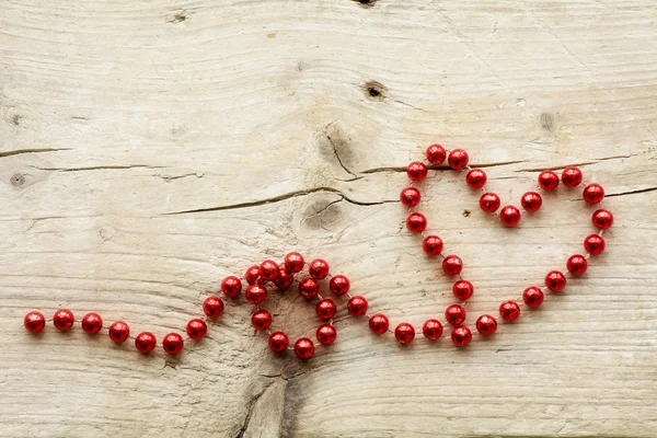 Garland of red christmas beads forming a heart shape on wood, lo — Stock Photo, Image