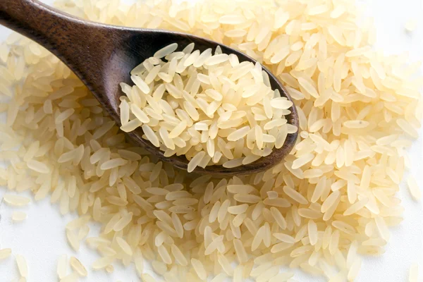 Small heap of parboiled rice with a wooden spoon on white, close — Stock Photo, Image