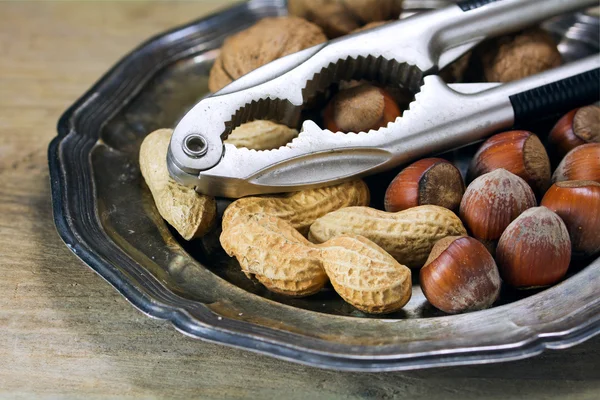 Hasselnötter, jordnötter och valnötter med en nötknäppare på en gammal silve — Stockfoto