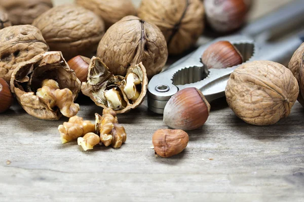 Nueces y avellanas con cascanueces sobre madera rústica, primer plano — Foto de Stock