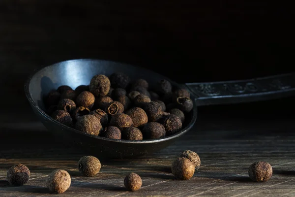 Allspice on an old metal spoon on a dark rustic wooden backgroun — Stock Photo, Image