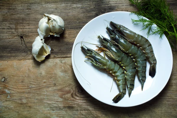 Gambas tigre negro crudo en un plato sobre una tabla de madera rústica, garl —  Fotos de Stock