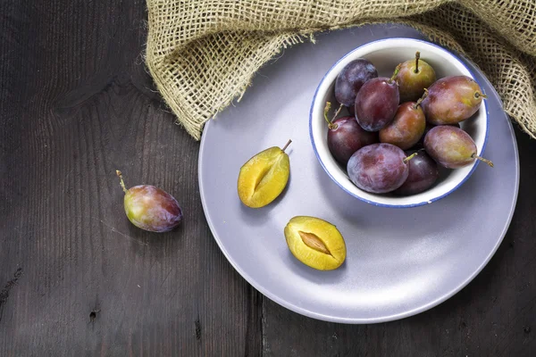 Ameixas frescas em um boliche e em uma chapa em uma mesa de madeira escura — Fotografia de Stock