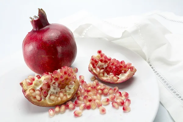 Granatapfel ganz und Stücke mit Körnern auf weißem Teller — Stockfoto