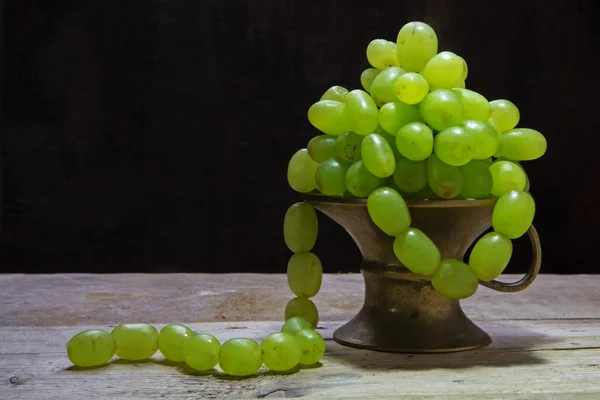 white grapes hanging like a necklace out of a brass bowl, vintag