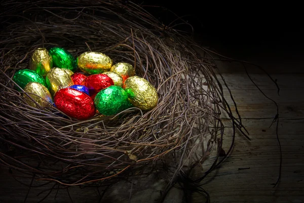 Osternest mit bunt verpackten Schokoladeneiern auf rustikalem Woo — Stockfoto