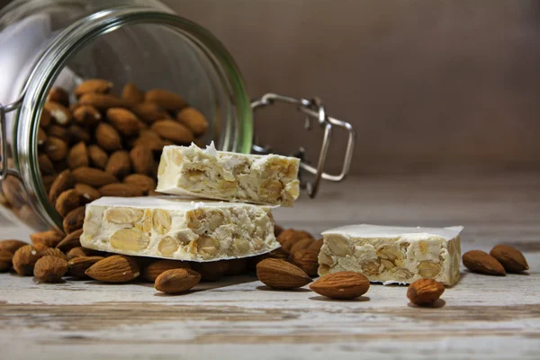 Torrone or nougat in front of a glass jar with almonds on a rust — Stock Photo, Image