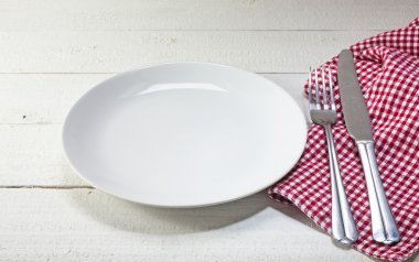 empty plate with cutlery and red white napkin on a white rustic 