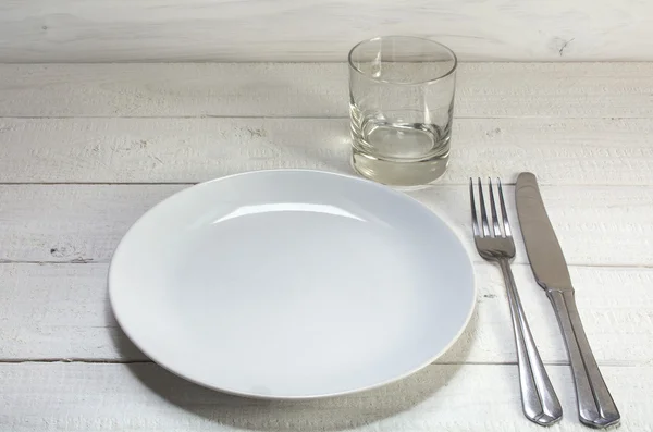 Plato blanco vacío con cuchillo, tenedor y vaso de beber en un blanco — Foto de Stock