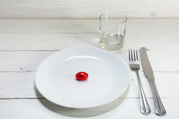 Plato blanco con un pequeño huevo de Pascua rojo, cuchillo, tenedor y drinki — Foto de Stock