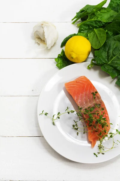 Raw salmon fillet with aromatic herbs, garlic, lemon and spinach — Stock Photo, Image