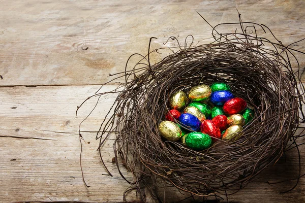 Osternest mit bunt verpackten Schokoladeneiern auf rustikalem Holz — Stockfoto