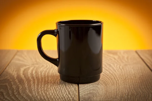 Black coffee mug on wooden table with yellow background — Stock Photo, Image