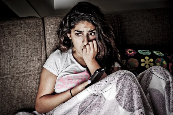 TV izlerken korkan genç bir kadın. Uzaktan kumanda ile kanepede oturan esmer kız