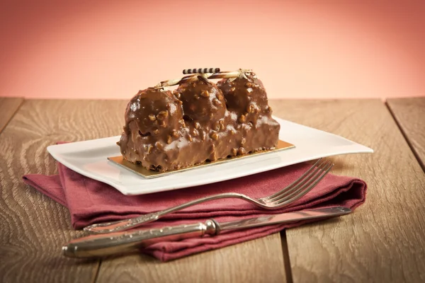 Profiteroles with chocolate and peanut cake pink background — Stock Photo, Image