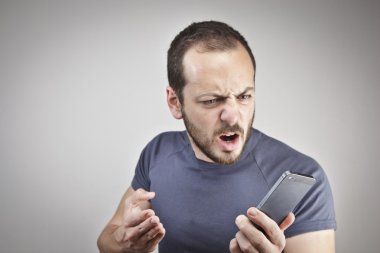 Angry young man while answering smart phone not understood clipart