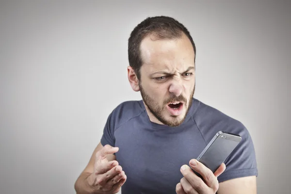 Angry young man while answering smart phone not understood — Stock Photo, Image