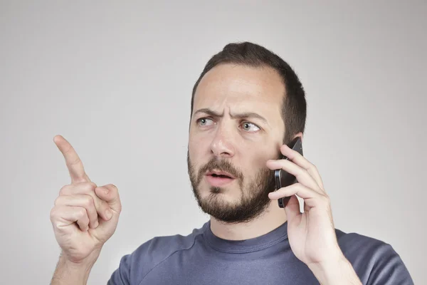 Jovem gesticulando enquanto atende telefone inteligente não entendido — Fotografia de Stock