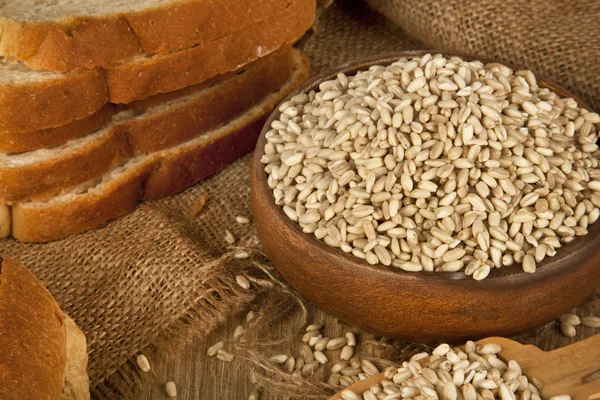 Wheat seeds in wooden plate and wood spoon with wooden background — Stock Photo, Image