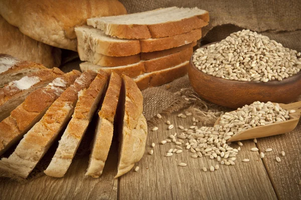 Pan de trigo, semillas de trigo y rebanadas de pan con fondo de madera —  Fotos de Stock