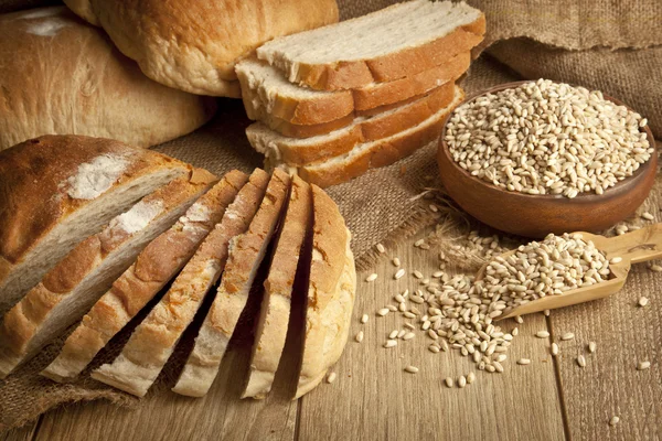 Celozrnný chléb, pšenice semena a plátky chleba s dřevěnou pozadí — Stock fotografie