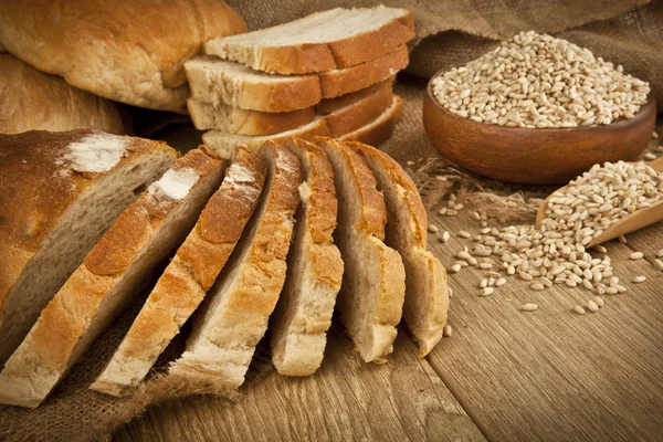 Pan de trigo, semillas de trigo y rebanadas de pan con fondo de madera —  Fotos de Stock