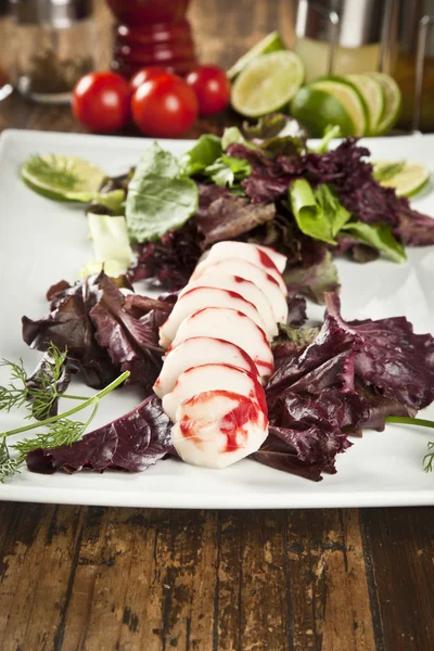 Lobster surimi slices on a platter with green and purple vegetables and limes — Stock Photo, Image