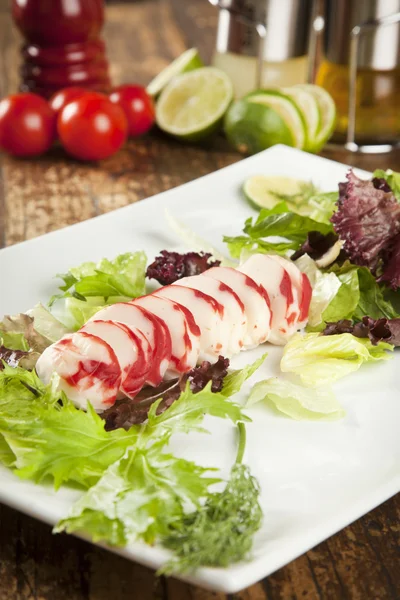 Lobster surimi slices on a platter with green and purple vegetables and limes — Stock Photo, Image