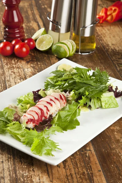 Langosta surimi rebanadas en un plato con verduras y limas verdes y moradas —  Fotos de Stock