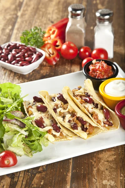 A plate of delicious tacos with lime, tomato, lettuce, and cheese. — Stock Photo, Image