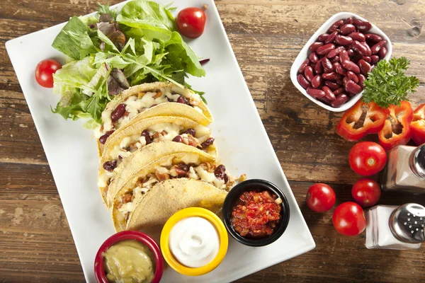 A plate of delicious tacos with lime, tomato, lettuce, and cheese. — Stock Photo, Image