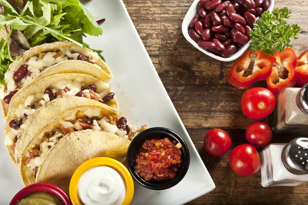 A plate of delicious tacos with lime, tomato, lettuce, and cheese. — Stock Photo, Image