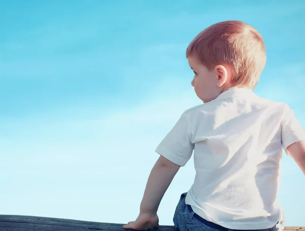 Little child boy sitting pensive looking away outdoors over blue — Stock Photo, Image