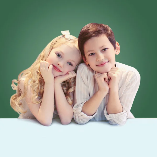 Retrato lindo sonriendo dos niños pupilos sentados a la mesa o — Foto de Stock