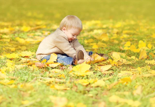 Счастливый симпатичный маленький ребенок, сидящий на траве и играющий с желтым — стоковое фото