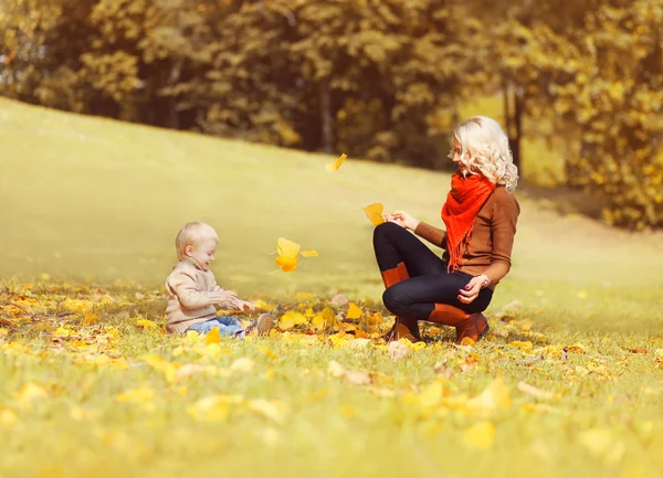 Feliz madre e hijo jugando juntos con hojas amarillas en gra — Foto de Stock