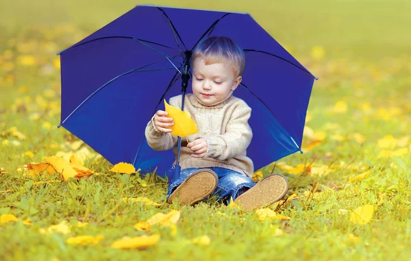 Маленький ребенок сидит на траве с зонтиком, играя с желтым — стоковое фото