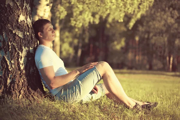 Relaxante homem sentado sob uma árvore com os olhos fechados meditando um — Fotografia de Stock