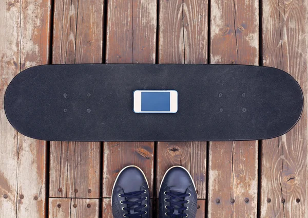 Skateboard with screen smartphone and sneakers over textured woo — Stock Photo, Image