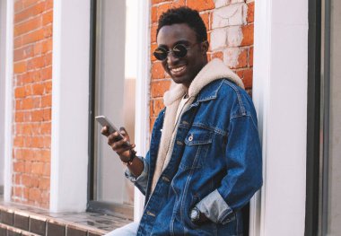 Duvarın arkasında akıllı telefonlu mutlu ve gülümseyen Afrikalı bir adamın portresi.