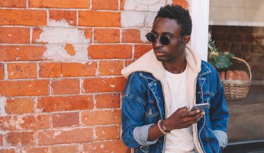 Akıllı telefonlu genç Afrikalı bir adamın portresi. Duvarın arkasından şehrin caddesine bakıyor.