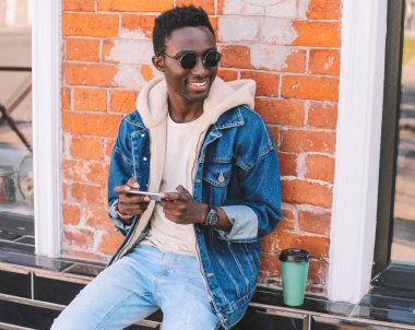 Duvarın arkasındaki duvarda akıllı telefon ve kahve fincanı olan Afrikalı genç bir adamın portresi.