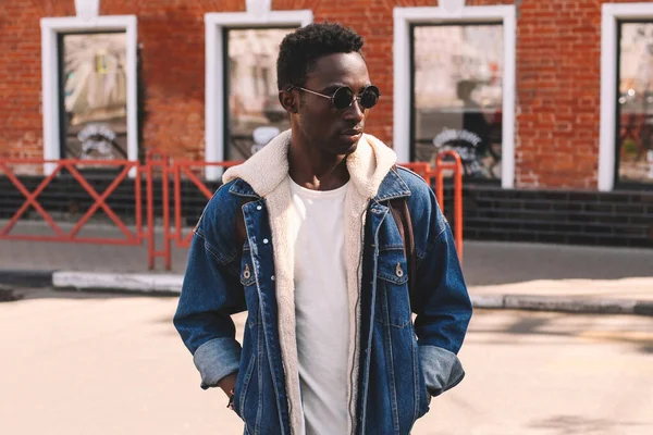 穿着斜纹棉布夹克 背包装束在城市街道上的时髦年轻非洲男模的肖像 — 图库照片