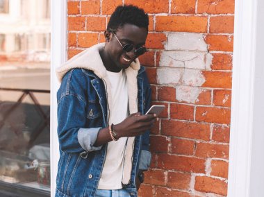 Duvarın arkasında akıllı telefonlu mutlu ve gülümseyen Afrikalı bir adamın portresi.