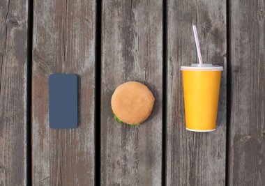 Fast food, sağlıksız diyet konsepti. Telefon, meyve suyu bardağı ve hamburgerle ahşap bir masa veya zemin üzerinde.