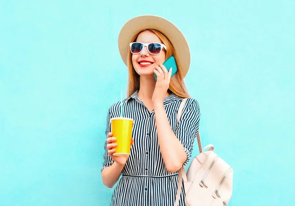 夏のポートレート幸せな笑顔の女性は 麦藁帽子をかぶってジュースのカップでスマートフォンを呼び出し 青い背景にバックパック — ストック写真
