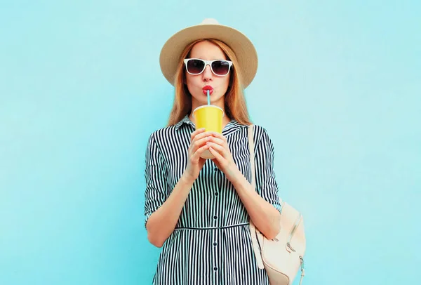 夏の丸いわら帽子をかぶってフルーツジュースを飲む美しい若い女性の肖像 青い背景に縞模様のドレス — ストック写真