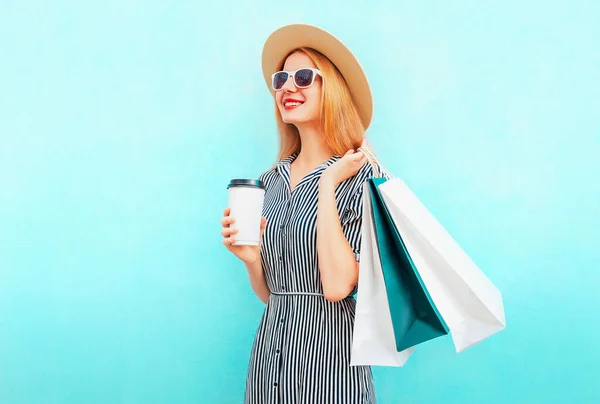 幸せな笑顔の女性でショッピングバッグやコーヒーカップを身に着けている夏のわらラウンド帽子 青の背景に黒の白いストライプのドレス — ストック写真