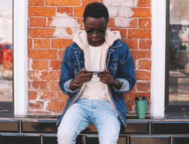 Duvarın arkasındaki duvarda akıllı telefon ve kahve fincanı olan Afrikalı genç bir adamın portresi.