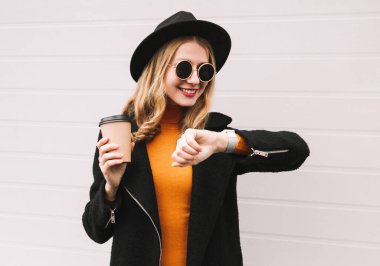 Genç ve mutlu bir kadının şık bir portresi. Bir fincan kahveyle akıllı saate bakıyor. Ses asistanı kullanıyor.